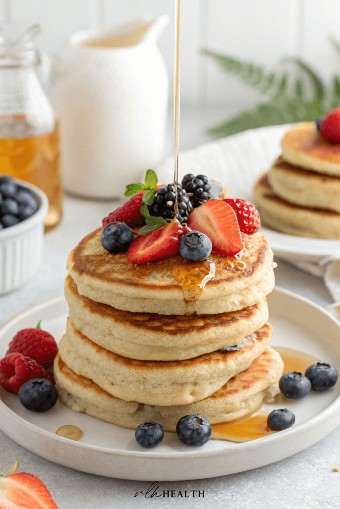 Stack of fluffy gluten-free protein pancakes drizzled with maple syrup and topped with fresh strawberries, blackberries, and blueberries.