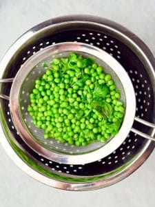 Drained peas, basil, and arugula in a colander.