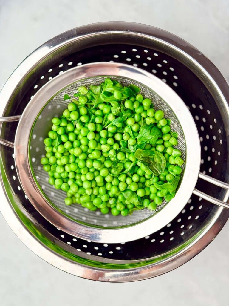 Drained peas, basil, and arugula in a colander.