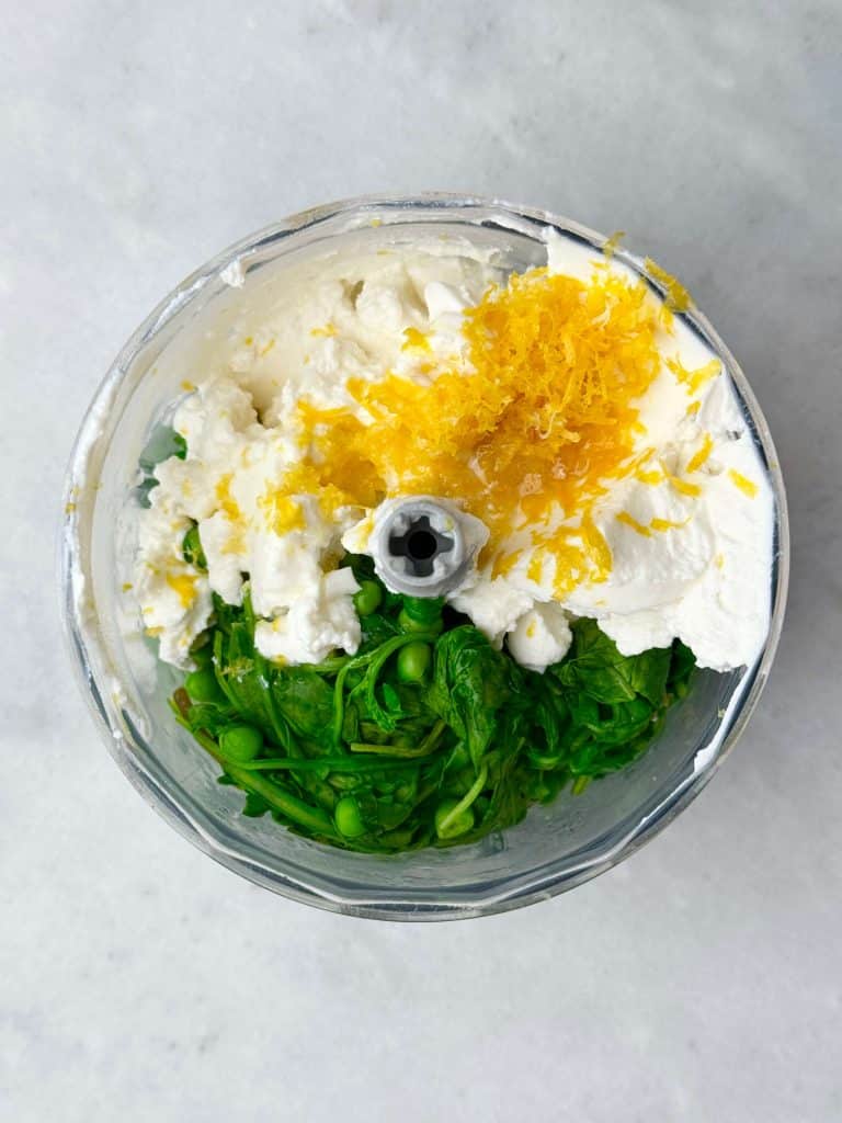 Blender filled with arugula, peas, ricotta, and lemon zest for green pea pasta sauce.