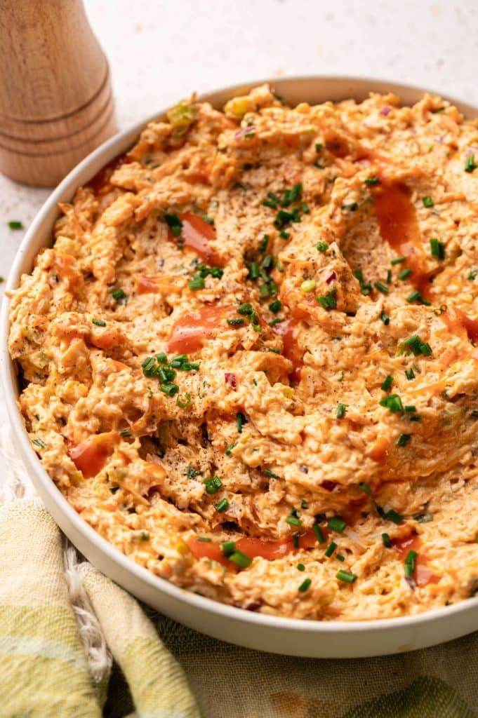 Close-up of creamy buffalo chicken salad topped with chives and a drizzle of hot sauce.