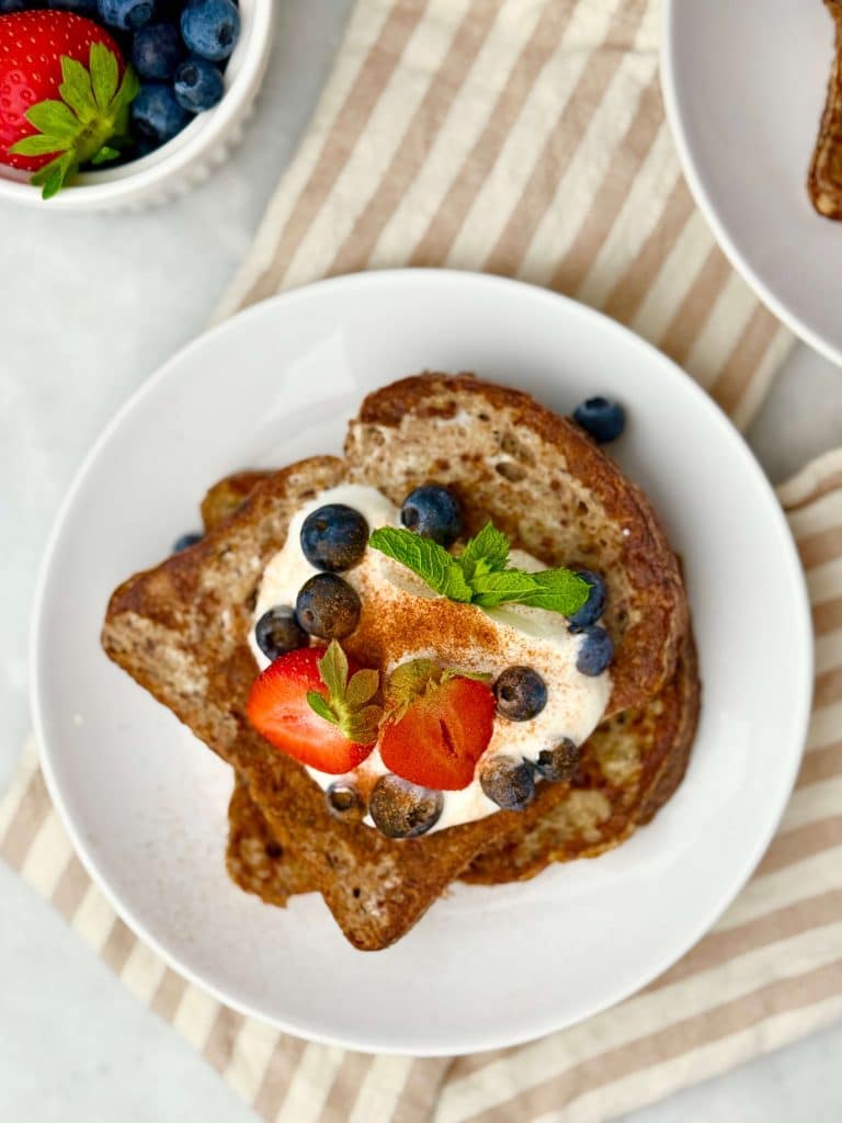 Top view of high protein French toast without protein powder garnished with yogurt, strawberries, blueberries, and fresh mint on a white plate.
