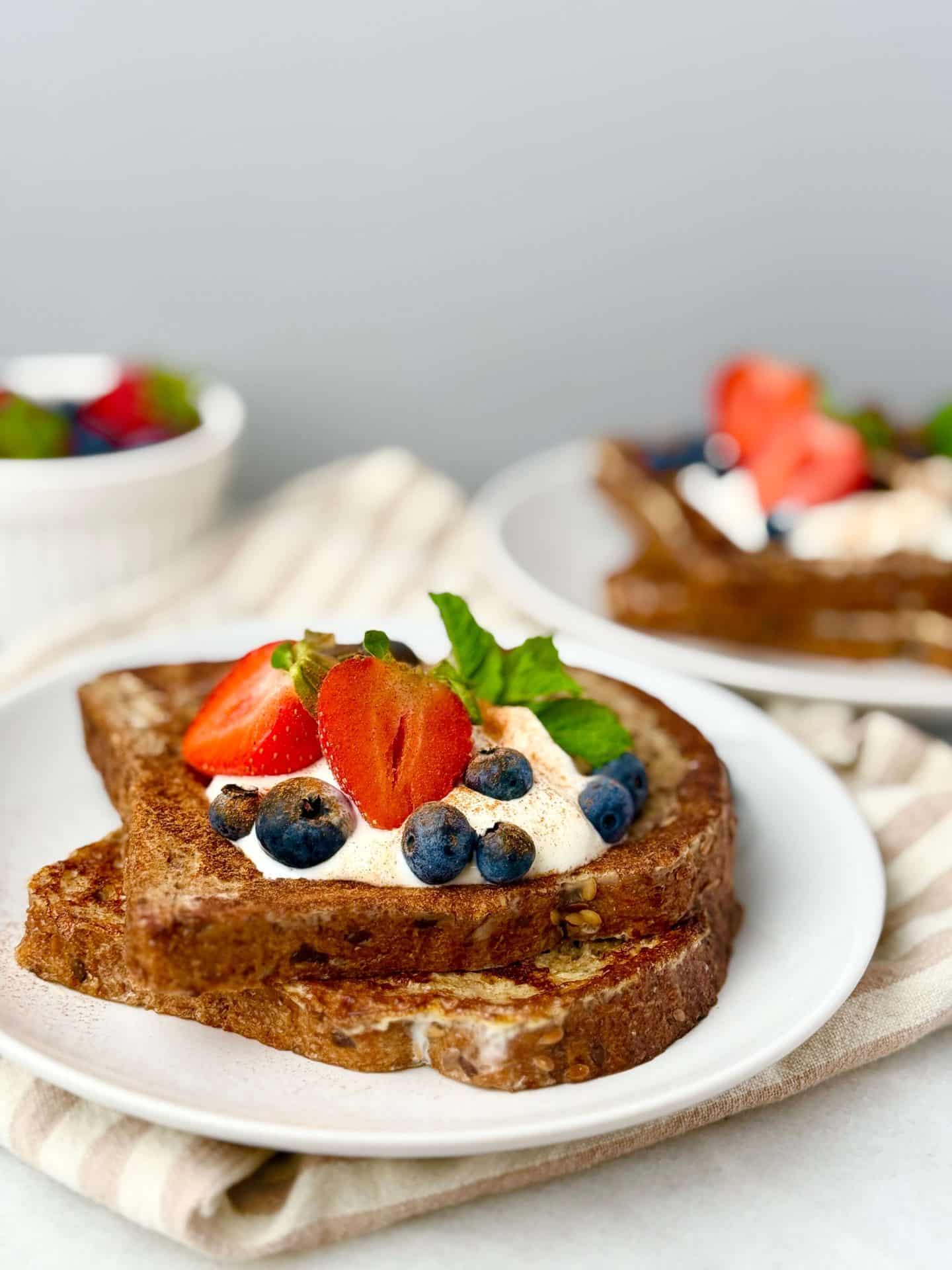 Close-up of high protein French toast without protein powder topped with Greek yogurt, fresh strawberries, blueberries, and mint on a white plate.