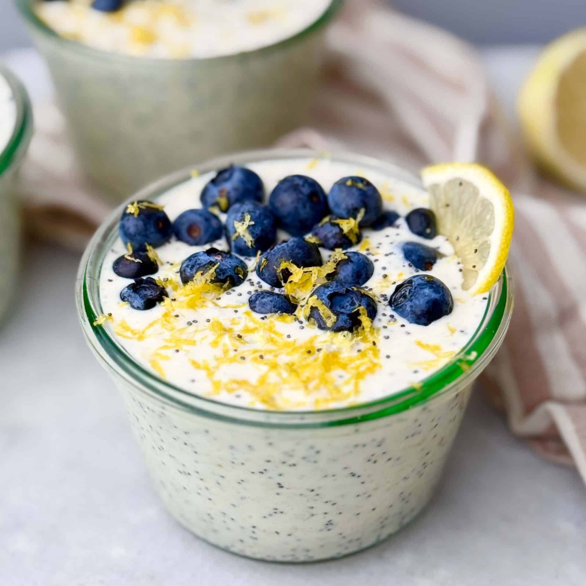 Close-up of a glass jar of lemon poppy seed overnight oats topped with fresh blueberries, lemon zest, and a lemon wedge