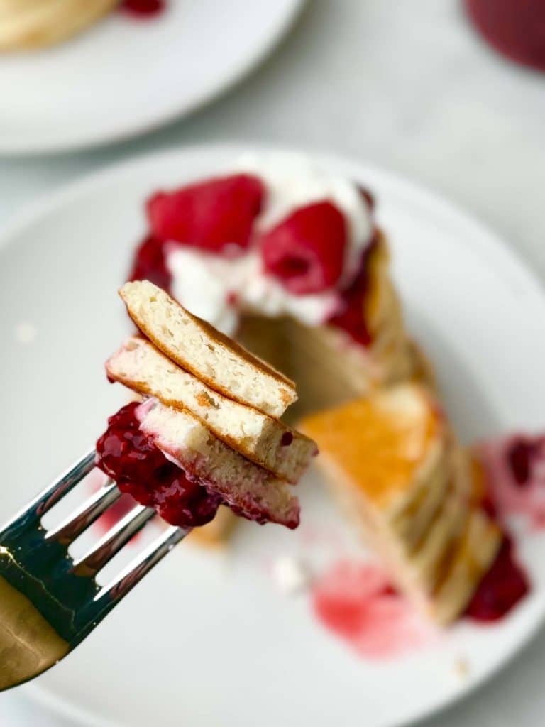 Fork holding bite of low calorie protein pancake with raspberry jam topping, showcasing fluffy texture and vibrant berry color.