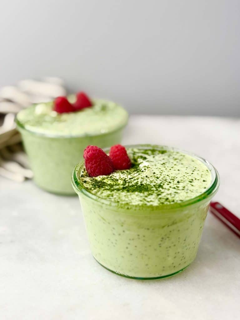 Side view of vibrant green matcha chia pudding with raspberries and matcha powder dusting, perfect high-protein breakfast.