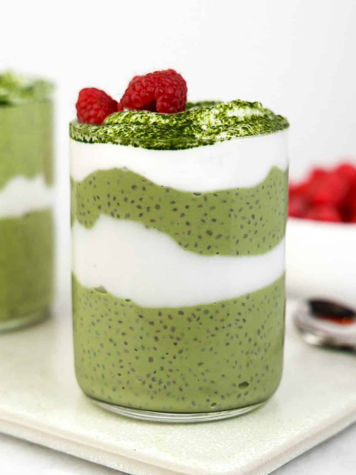 Layered matcha chia pudding in a glass topped with matcha powder and fresh raspberries