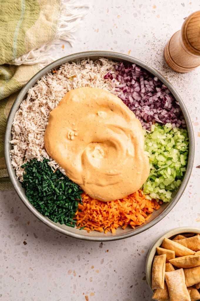 Creamy buffalo dressing poured over shredded chicken and vegetables in a bowl.