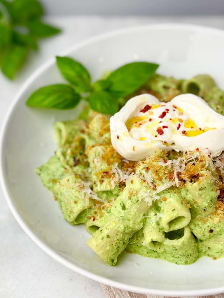 Close-up of rigatoni coated in lemony green pea pasta sauce, garnished with burrata and chili flakes. Easy lemon pea pasta for weeknight meals.