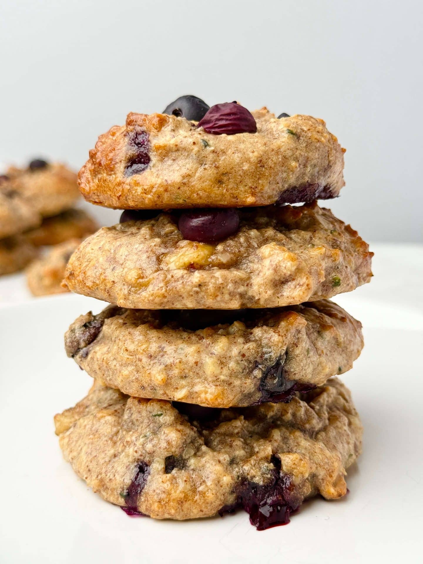 Stack of healthy high protein breakfast cookies with blueberries on a white plate. Soft, gluten-free, dairy-free cookies perfect for meal prep.