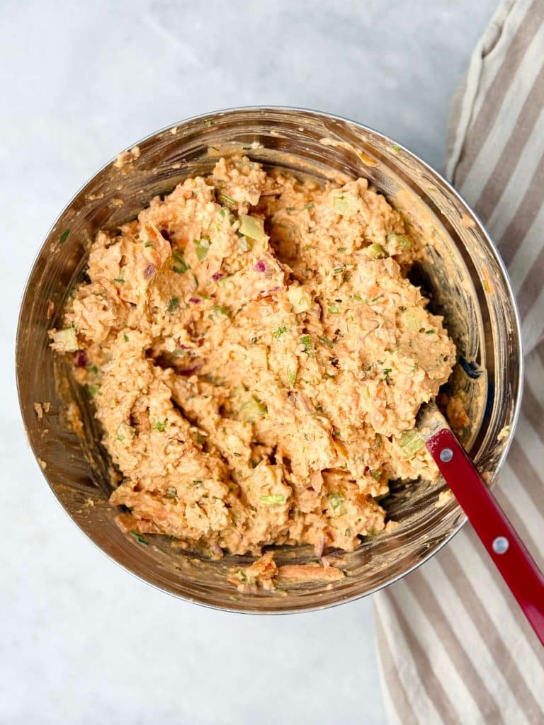 Healthy buffalo chicken salad fully combined with creamy dressing and colorful veggies in a mixing bowl.