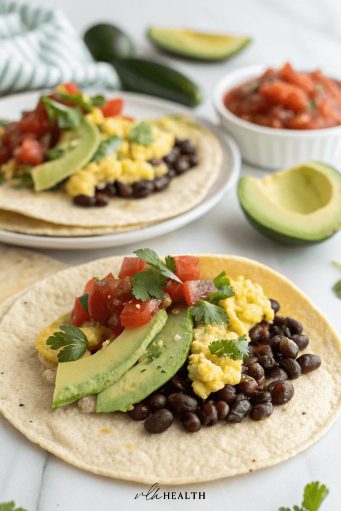 Two corn tortillas filled with scrambled eggs, black beans, avocado slices, salsa, and fresh cilantro.
