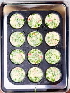 Unbaked Starbucks egg white bites mixture in muffin tin, spinach and red peppers visible before baking in water bath.