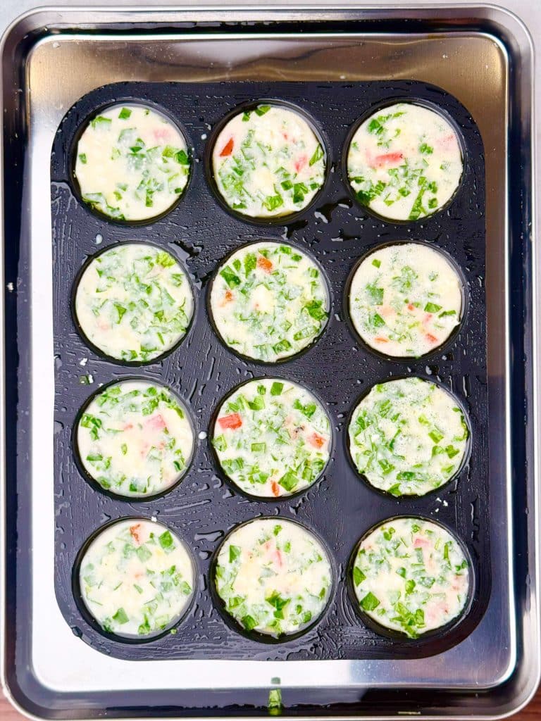 Unbaked Starbucks egg white bites mixture in muffin tin, spinach and red peppers visible before baking in water bath.