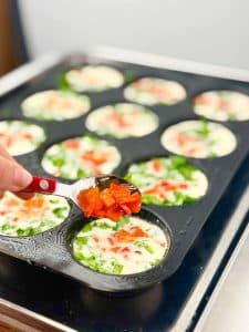 Adding roasted red pepper pieces to Starbucks egg white bite mixture in muffin tin before baking for bright color and flavor.