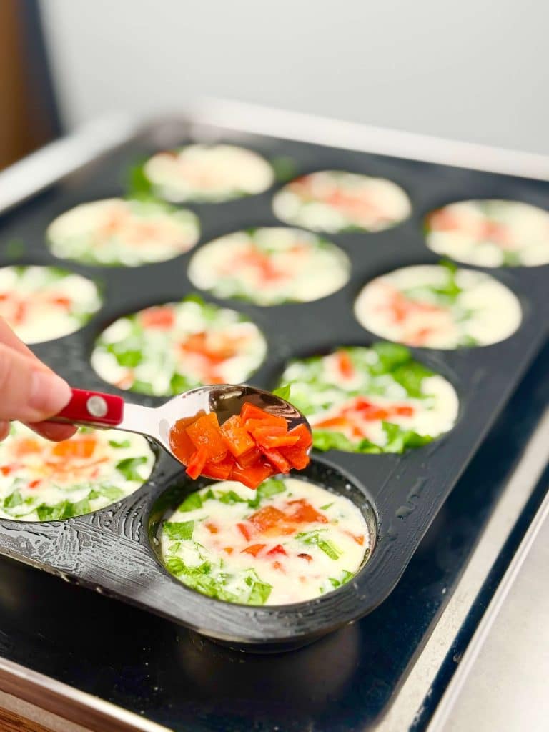 Adding roasted red pepper pieces to Starbucks egg white bite mixture in muffin tin before baking for bright color and flavor.
