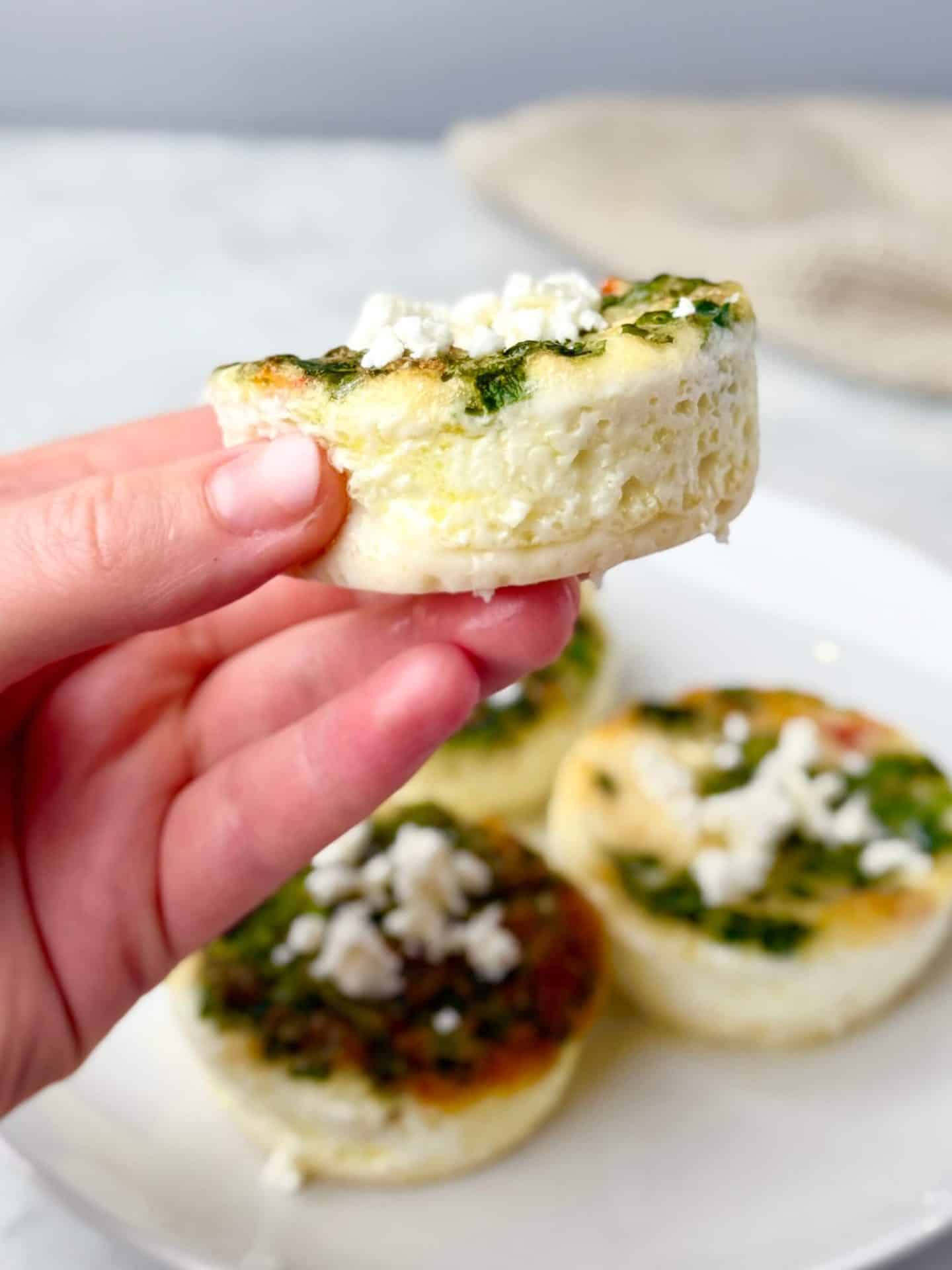 Hand holding a fluffy Starbucks egg white bite with spinach and feta, showing soft texture and roasted red pepper inside.
