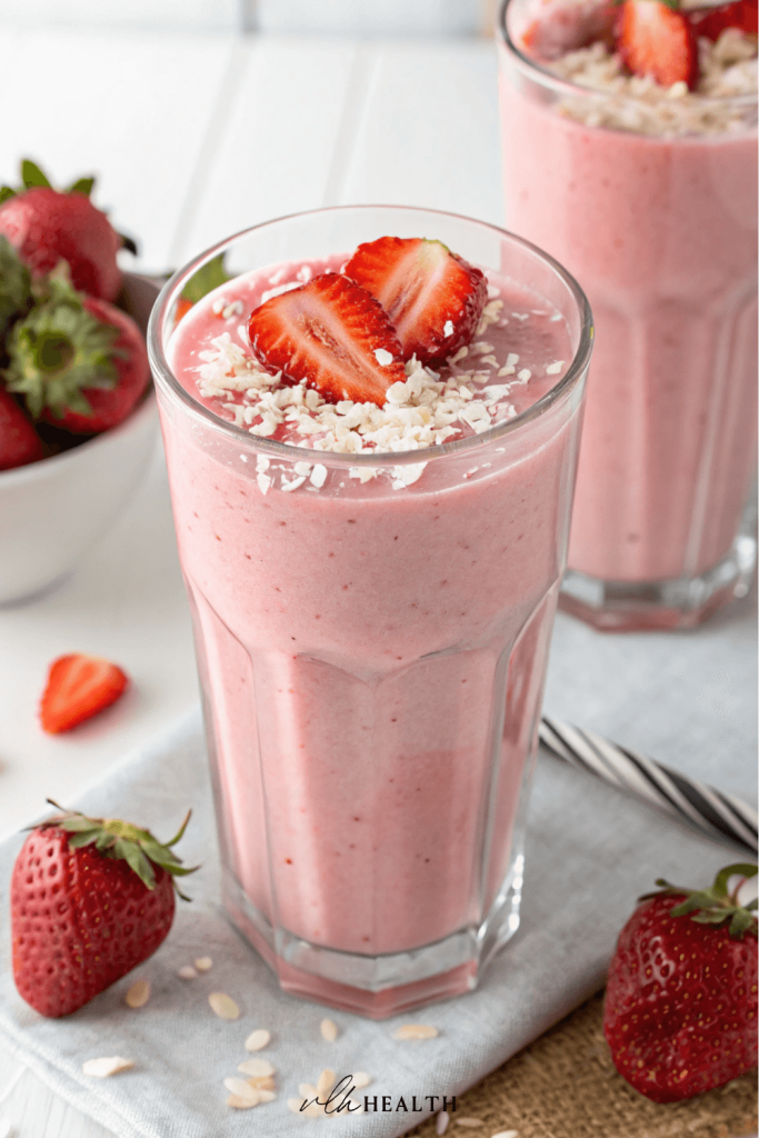 Tall glass of creamy pink strawberry smoothie topped with fresh strawberry slices and shredded coconut.