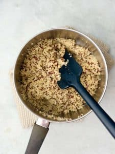 Pot of cooked tricolor quinoa with a black spatula, ready to add to spinach strawberry salad.