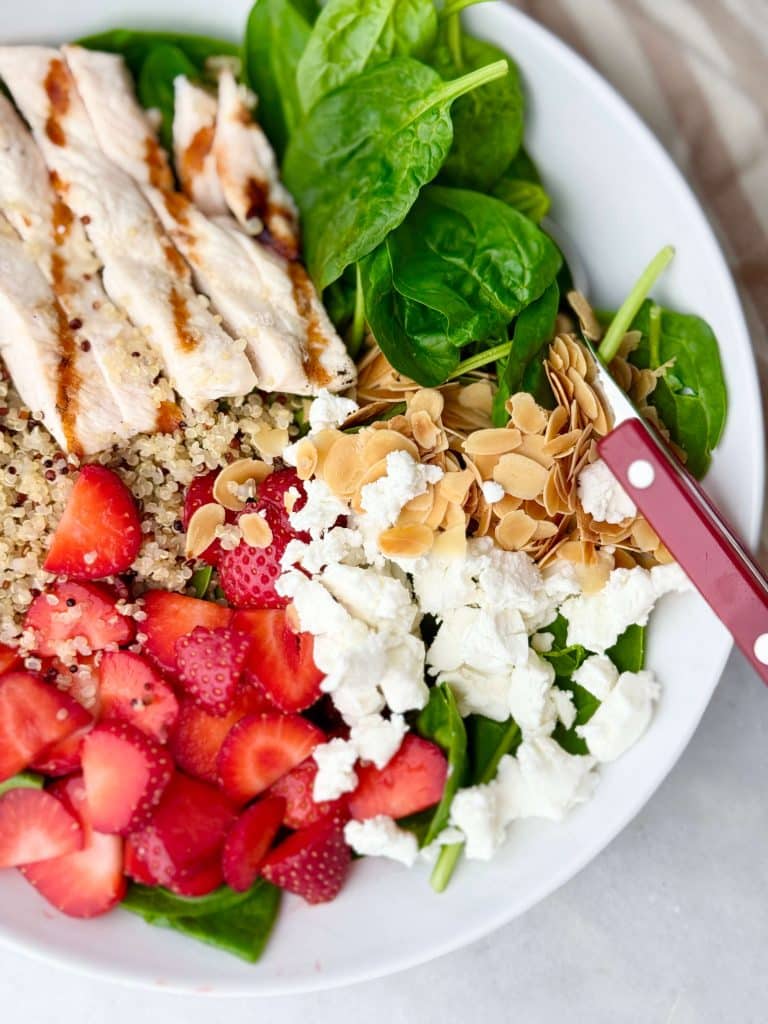 Close-up of strawberry spinach salad showing juicy strawberries, creamy goat cheese, grilled chicken, and crunchy sliced almonds.