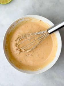 Bowl of creamy chipotle crema made with Greek yogurt, lime juice, and adobo sauce, whisked until smooth, ready to drizzle over sheet pan chicken fajitas.