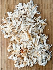 Close-up of freshly shredded chicken breast on a wooden cutting board, ready to add back into the soup.