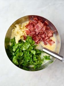 Bowl filled with chopped spinach, cooked turkey bacon, and frozen hash browns ready to be mixed into a high protein cottage cheese egg bake.