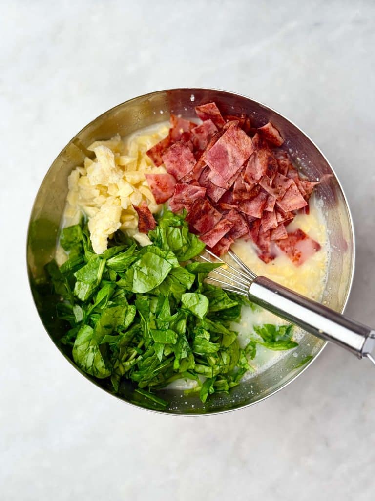 Bowl filled with chopped spinach, cooked turkey bacon, and frozen hash browns ready to be mixed into a high protein cottage cheese egg bake.
