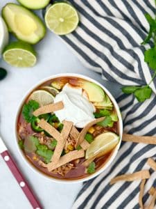 Crockpot chicken tortilla soup served with creamy yogurt, fresh cilantro, avocado, lime wedges, and crunchy tortilla strips.