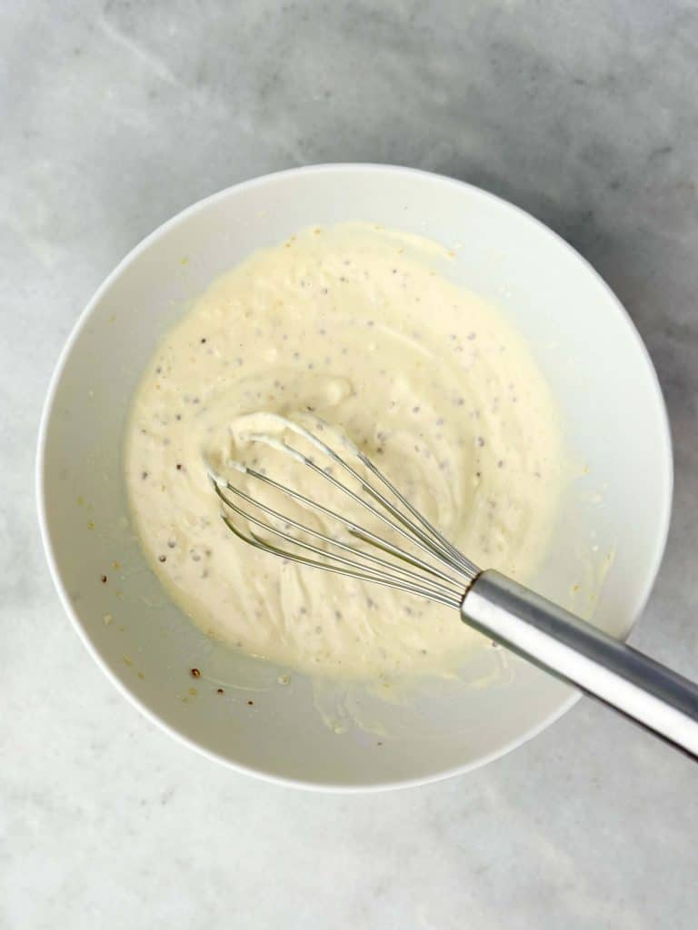 Creamy Greek yogurt and mayo dressing with mustard and pickle juice whisked in a white bowl on marble countertop.