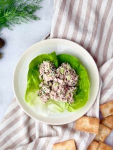 Healthy dill pickle tuna salad served in butter lettuce cups with crackers on the side, styled on a striped napkin.