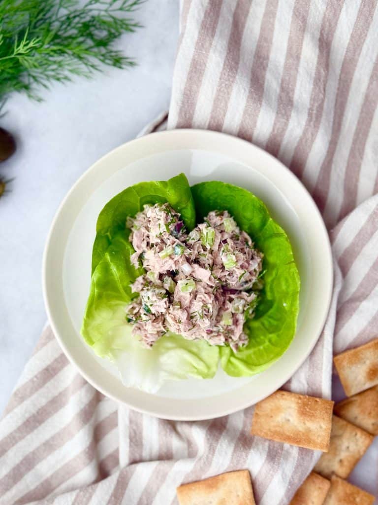 Healthy dill pickle tuna salad served in butter lettuce cups with crackers on the side, styled on a striped napkin.