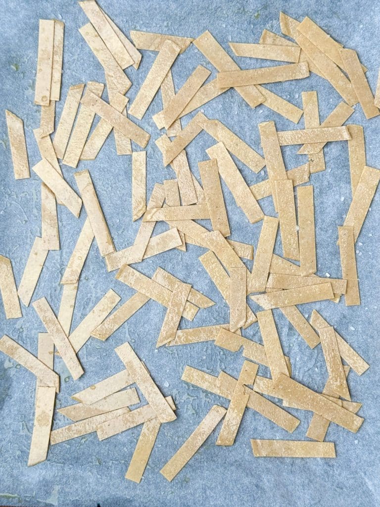 Unbaked tortilla strips arranged on a baking sheet, lightly oiled and ready to crisp in the oven.