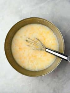 Mixing bowl with whisk combining egg whites, cottage cheese, and shredded cheese as the base for a high protein egg bake casserole.