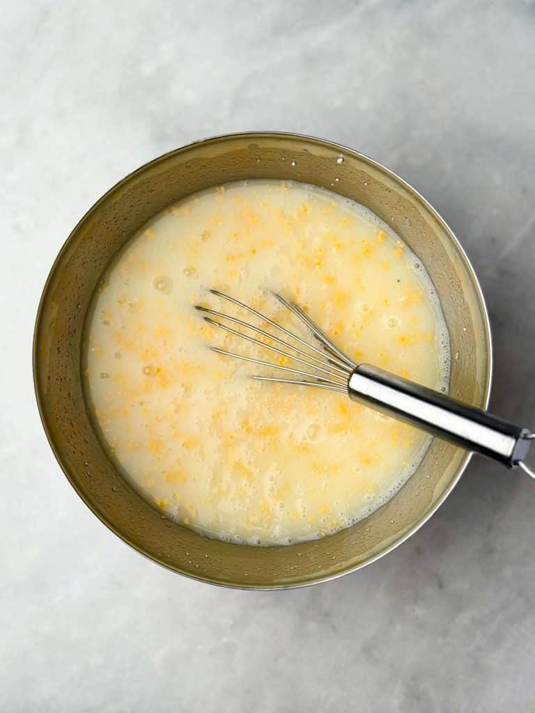 Mixing bowl with whisk combining egg whites, cottage cheese, and shredded cheese as the base for a high protein egg bake casserole.
