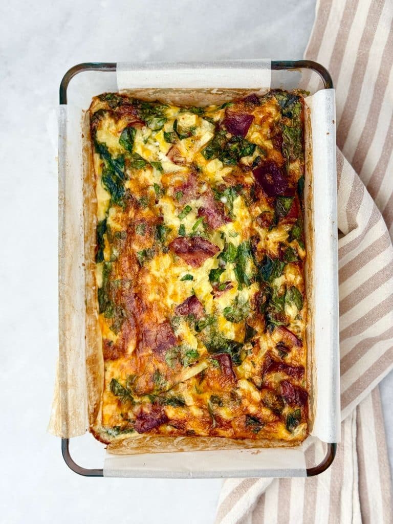 Freshly baked egg casserole with cottage cheese, spinach, and turkey bacon in a parchment-lined glass baking dish.