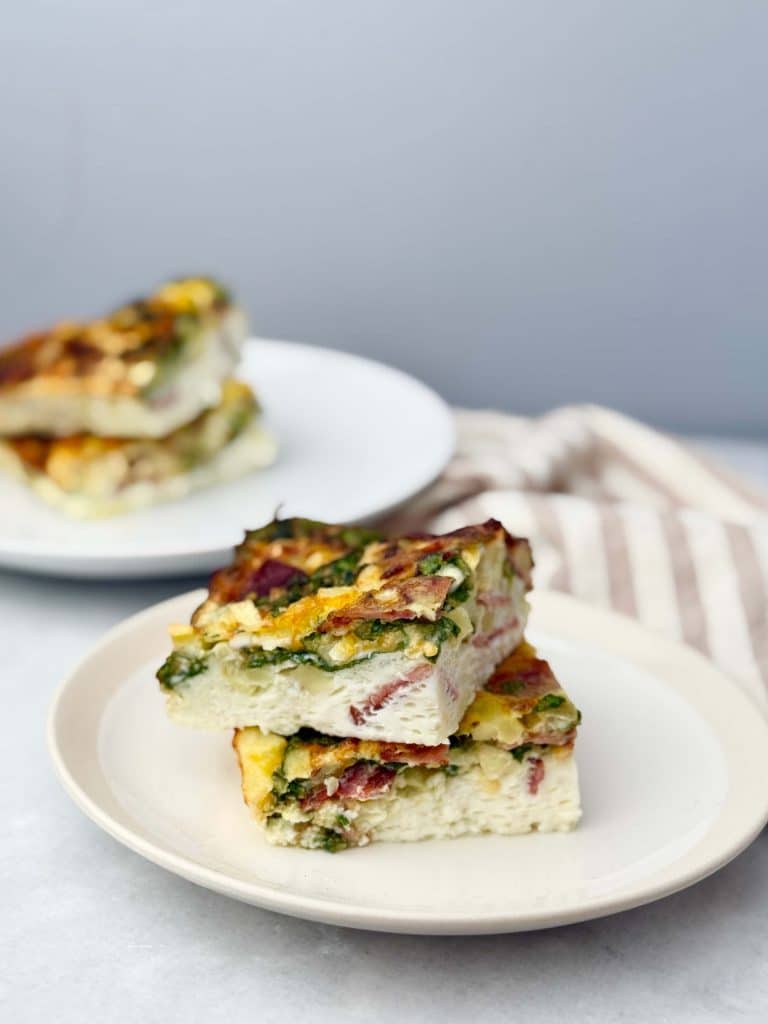 Two stacked slices of high protein egg bake with cottage cheese, turkey bacon, and spinach served on a white plate for breakfast meal prep.