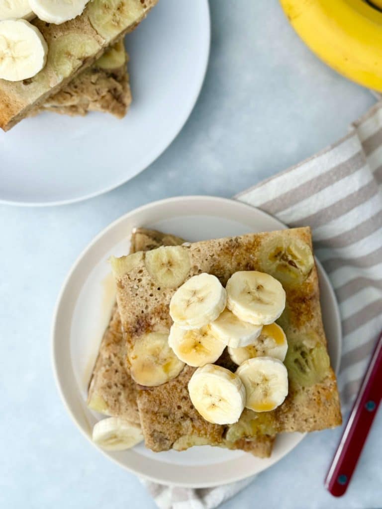 Overhead view of banana protein pancakes stacked on a plate and topped with fresh banana slices.