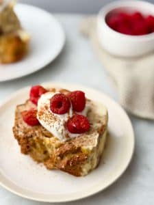 A thick slice of high protein French toast bread pudding on a plate with yogurt and fresh raspberries.