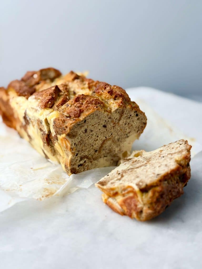 A loaf of high protein French toast bread pudding sliced on parchment paper, showing its golden crust and soft, custardy center.