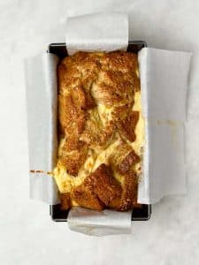 Overhead view of high protein French toast bread pudding baked in a parchment-lined loaf pan with a golden brown top.