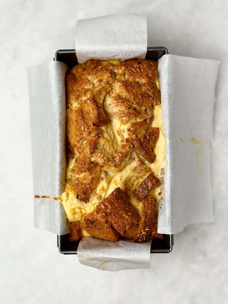 Overhead view of high protein French toast bread pudding baked in a parchment-lined loaf pan with a golden brown top.