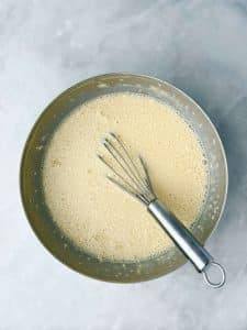 Mixing bowl filled with the custard mixture for high protein French toast bread pudding with a whisk inside.