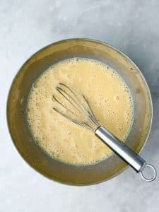 Whisk in a bowl with eggs, mashed banana, milk, and vanilla for sheet pan banana protein pancake batter.