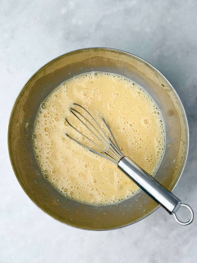 Whisk in a bowl with eggs, mashed banana, milk, and vanilla for sheet pan banana protein pancake batter.