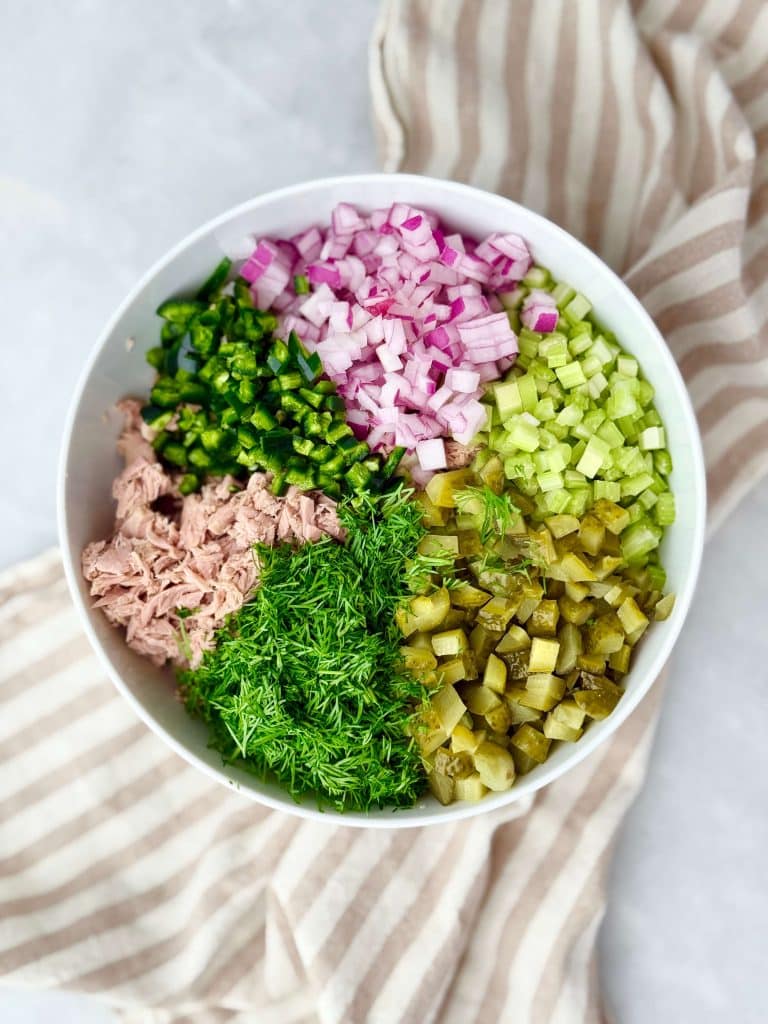 Bowl filled with chopped pickles, celery, red onion, jalapeño, fresh dill, and tuna arranged separately for healthy dill pickle tuna salad.
