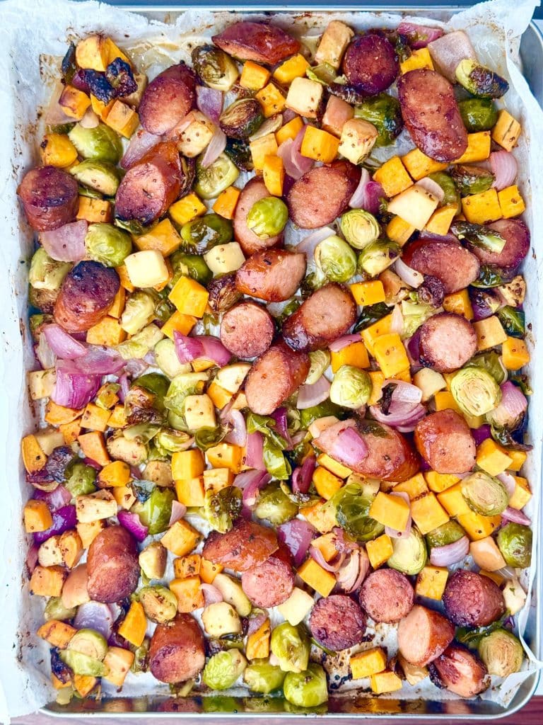 Fully cooked fall sausage and veggie sheet pan with golden brown sausage, sweet potatoes, and Brussels sprouts.