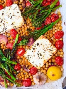 Sheet pan filled with roasted chickpeas, blistered tomatoes, broccolini, red onions, garlic, lemon, and golden baked feta