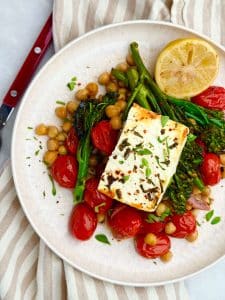 Overhead view of Mediterranean baked feta with chickpeas, tomatoes, and broccolini on a white plate with striped linen