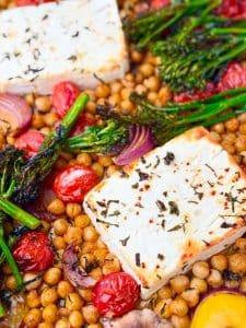 Golden baked feta with chickpeas, tomatoes, red onion, and charred broccolini on a parchment-lined sheet pan